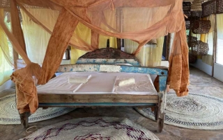 blue and white kings size bed made of old boats with orange mosquito net on floor with 3 round mats