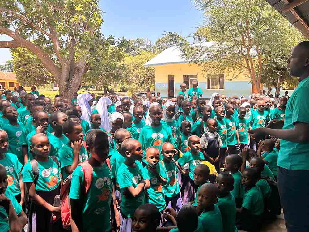 Children standig outside in an audience listening to teacher about beach clean up bottle project in Pangani, Tanzania, Africa